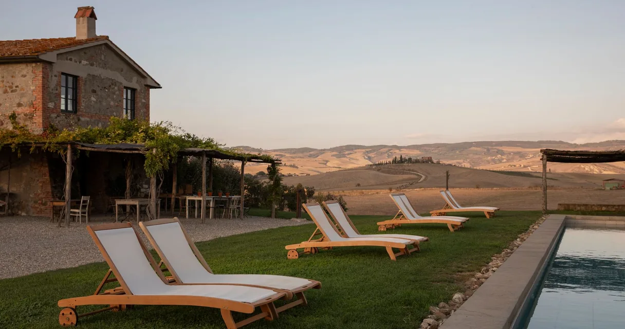 Espreguiçadeiras à beira da piscina de uma hospedagem rural com vista para o campo